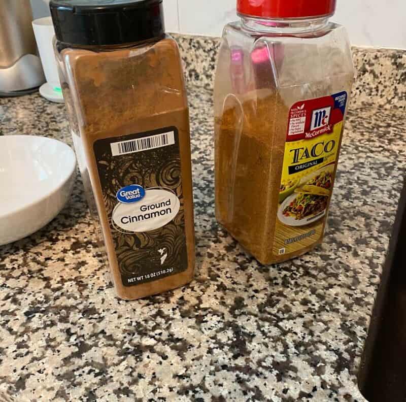 Ground cinnamon bottles on a kitchen countertop, one with a black lid and the other with a red lid.