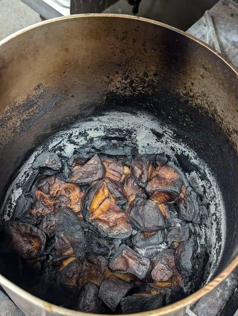 Burnt food in a blackened pot, with charred pieces and black residue.