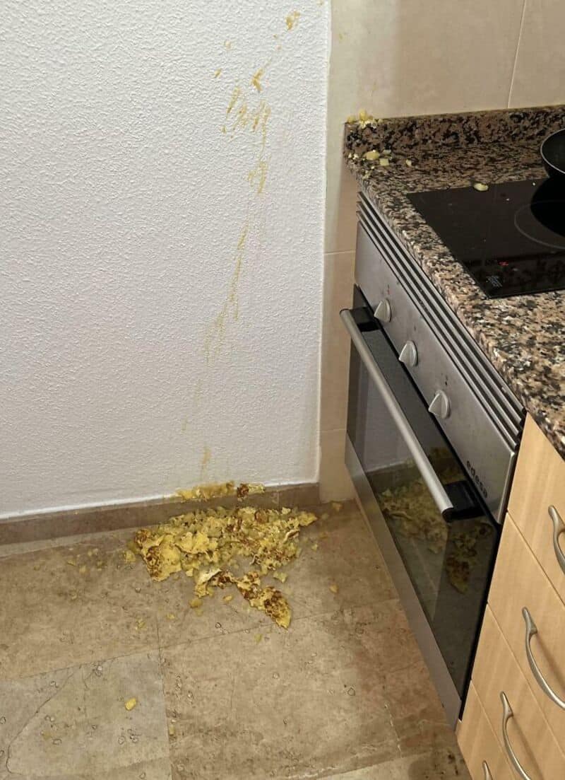 Messy kitchen corner with spilled food on the floor and wall.