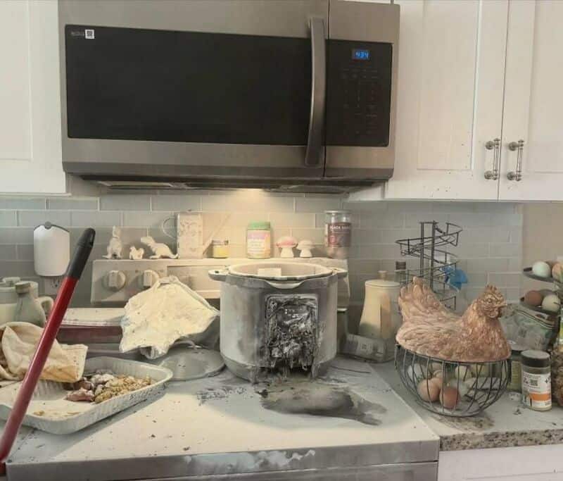 Burned microwave with soot on the kitchen counter in a messy kitchen.