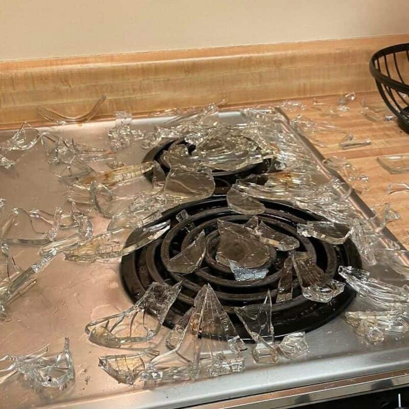 Broken glass on a stove in a kitchen, with shards scattered around.