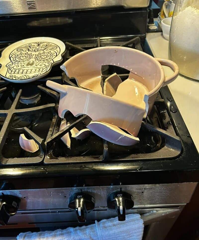 Broken ceramic bowl on stove with shattered pieces around it.