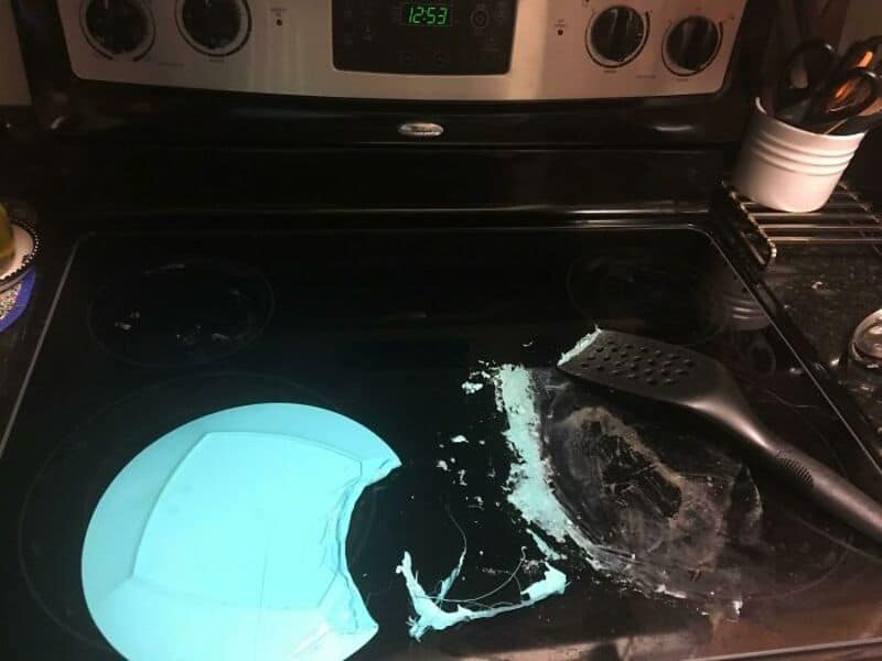 Broken blue plate on stove with spilled flour and a spatula nearby.