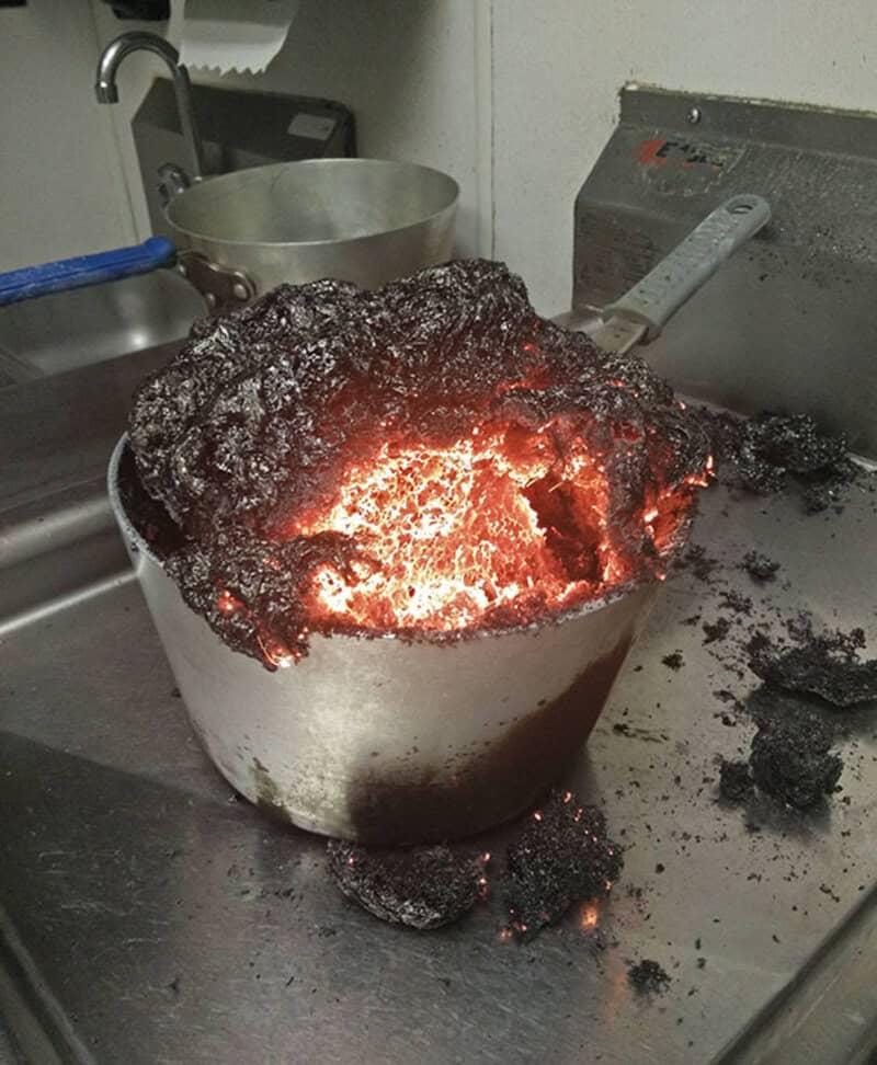 Burnt pot with charred contents and glowing embers, on a kitchen stove.