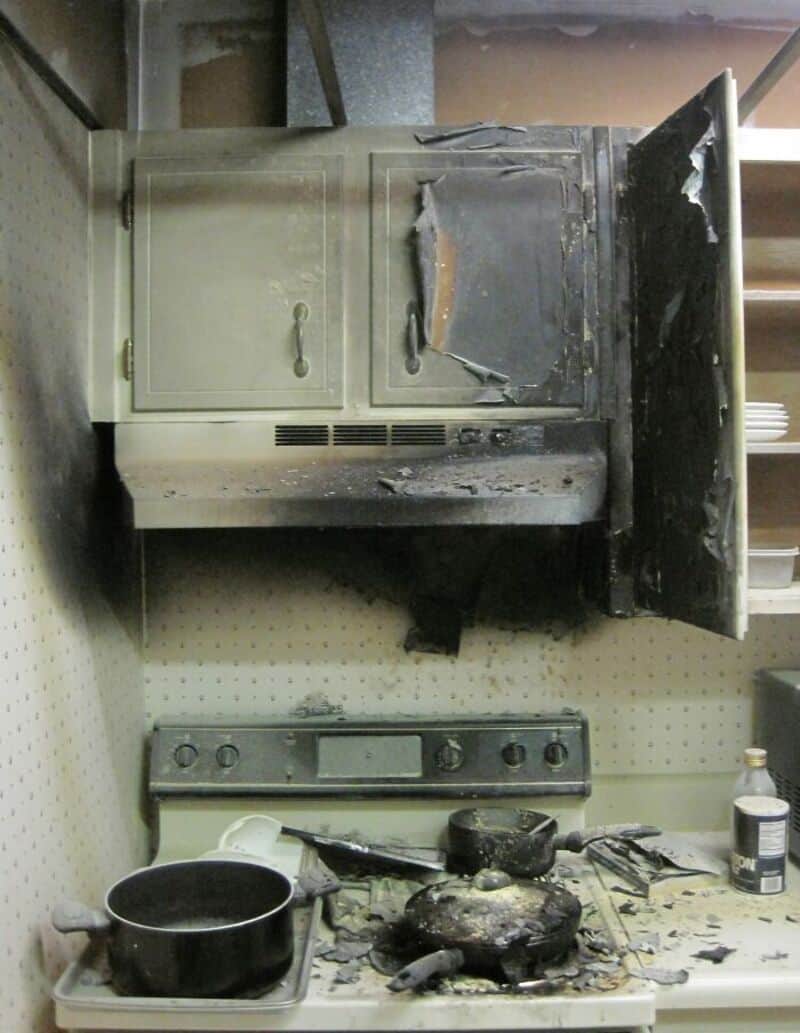 Burned and damaged stove and oven in a kitchen, with a burnt pot and soot.