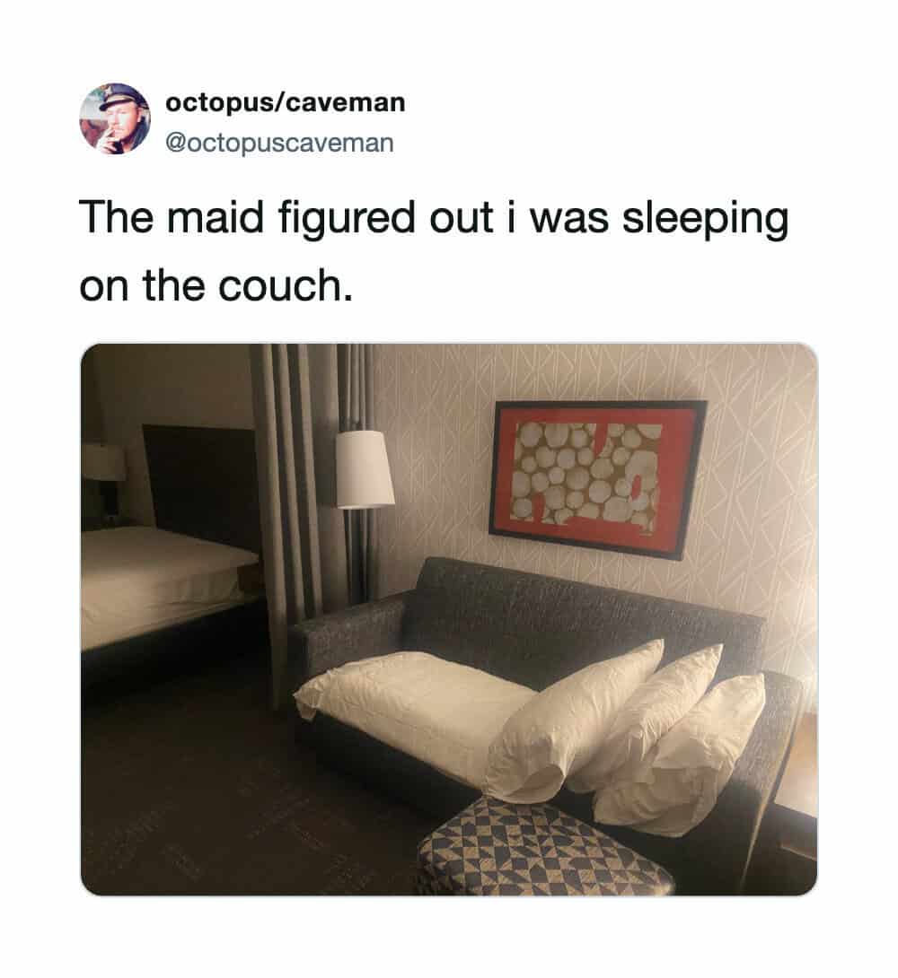 A couch with a pillow and a blanket, a bed in the background, and a framed picture on the wall.