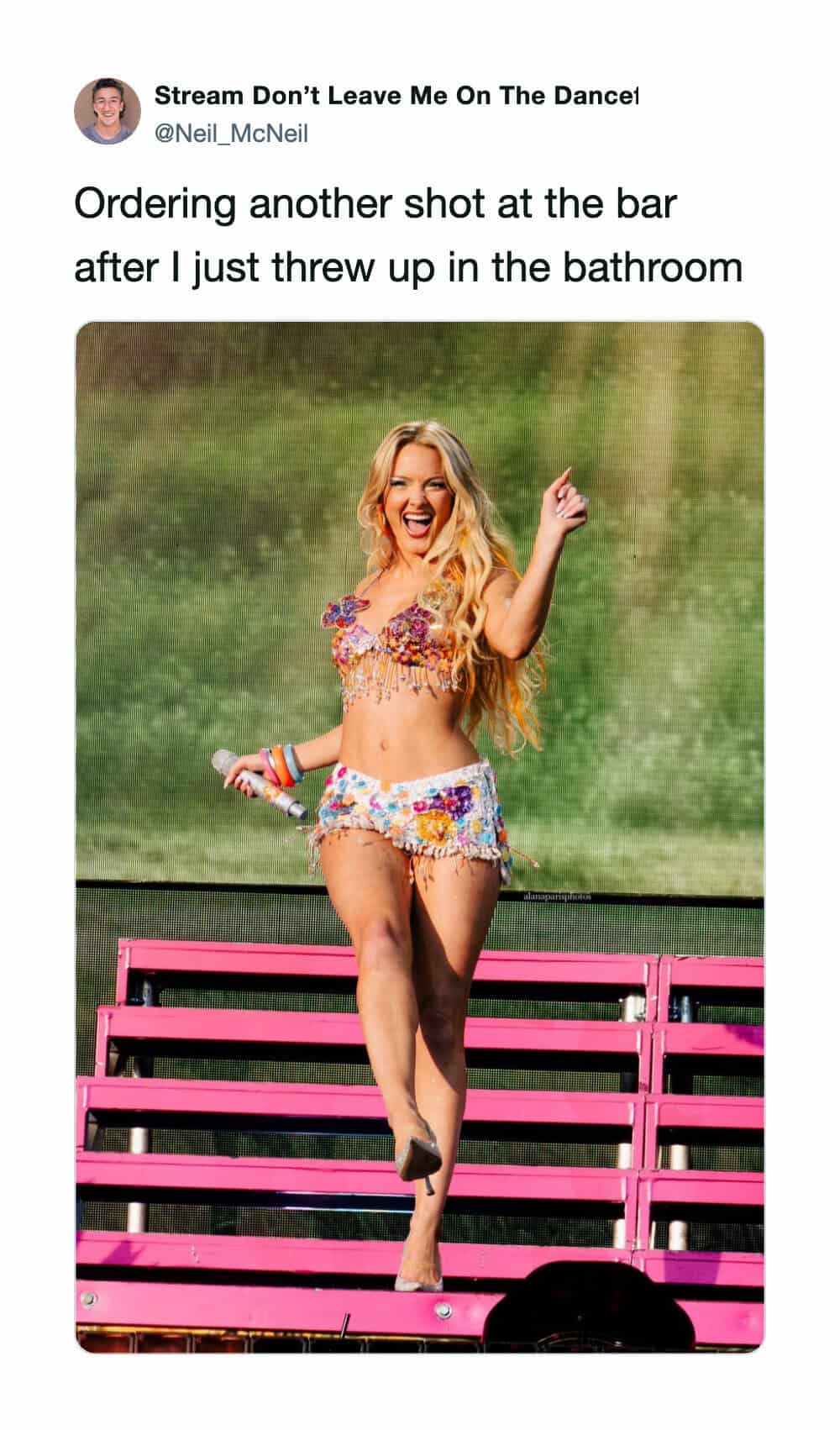 Woman dancing on stage with a microphone, wearing colorful shorts and a crop top.