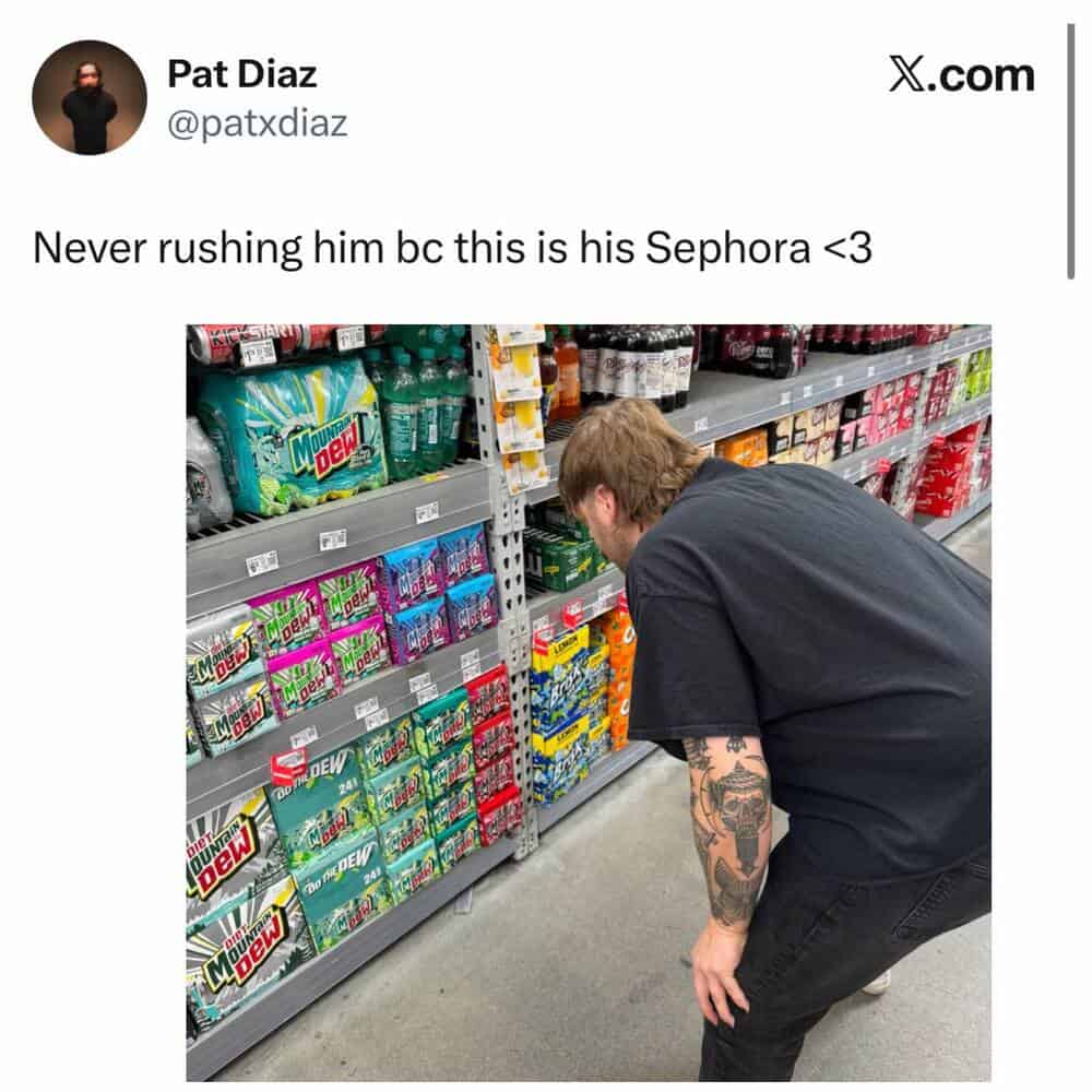 Man shopping for soda in a store aisle, bending down to pick a drink.