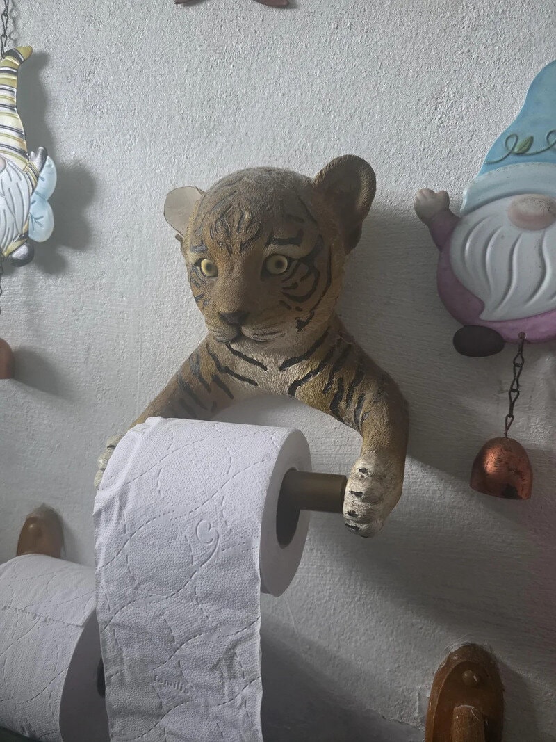 A tiger plush toy with a toilet paper roll in its paw, mounted on the wall.
