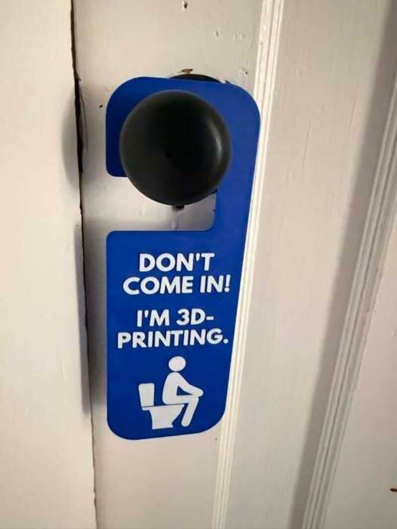 Sign says 'Don't come in! I'm 3D-printing' with a person sitting on a toilet.
