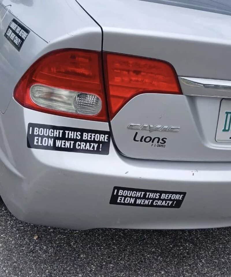 Car with two stickers saying "I BOUGHT THIS BEFORE ELON WENT CRAZY!".