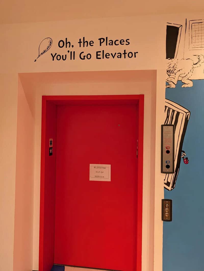 Red elevator door with a sign and humorous wall art above it.