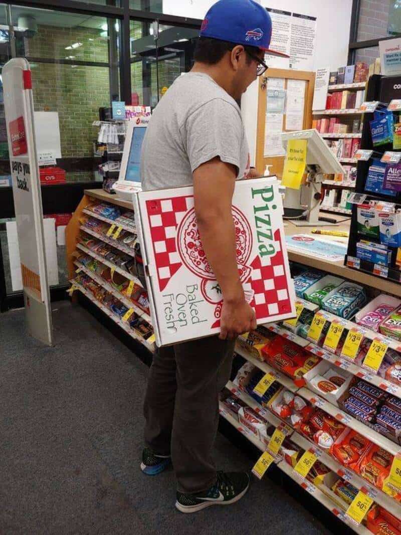 Man in a store holding a pizza box with a checkered pattern and the word 'Pizza'.