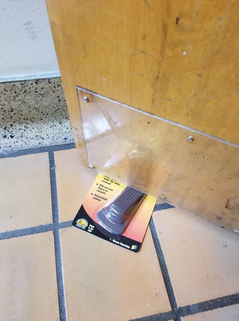 A card with a black object is stuck under a wooden door, blocking it.