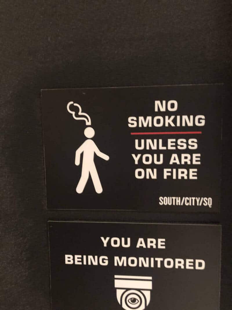 No smoking unless you are on fire sign with a smoking figure and surveillance camera.