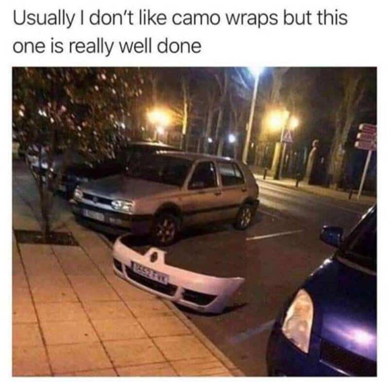 Car with a camo wrap and a detached front bumper on the sidewalk.