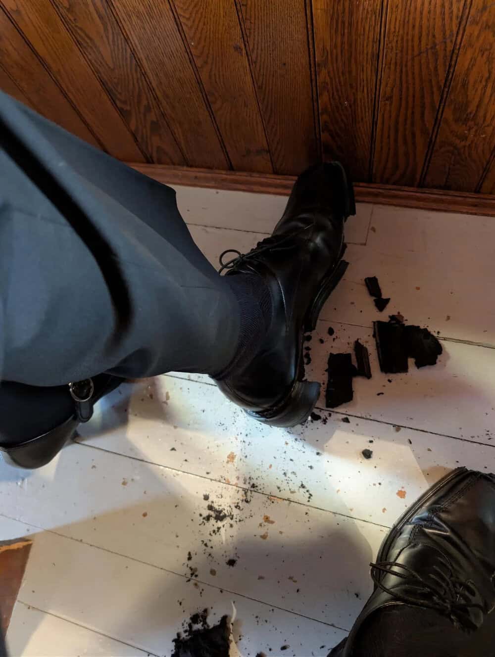 Person's foot in a black boot stepping on broken chocolate cookies on the floor.