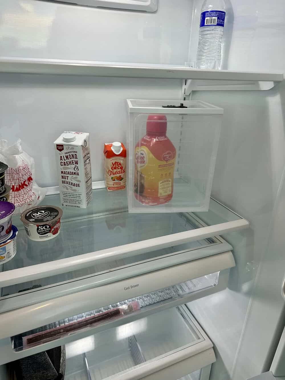 Inside a refrigerator with various drinks and a water bottle on top shelf.