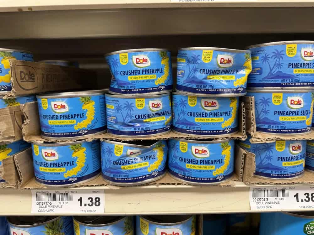 Cans of Dole crushed pineapple on store shelf.