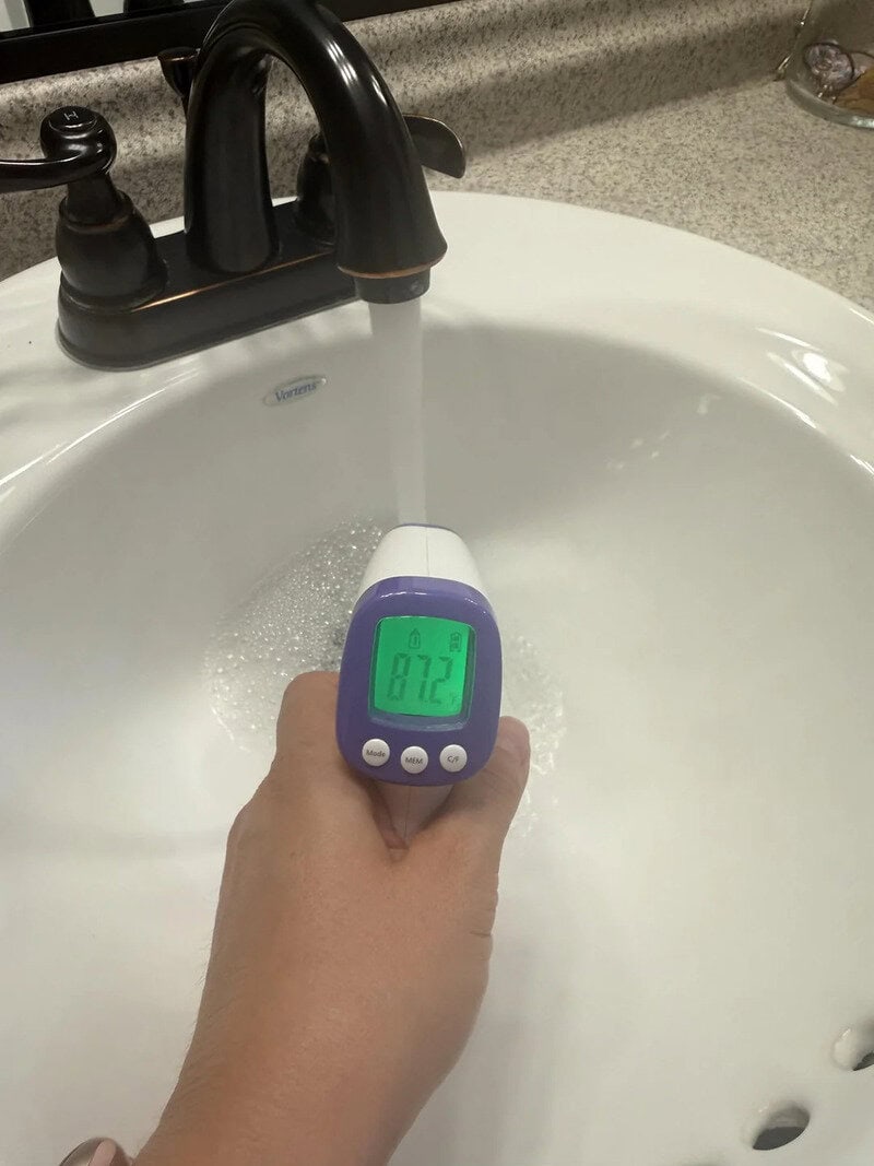 Person measuring water temperature in sink with a digital thermometer.