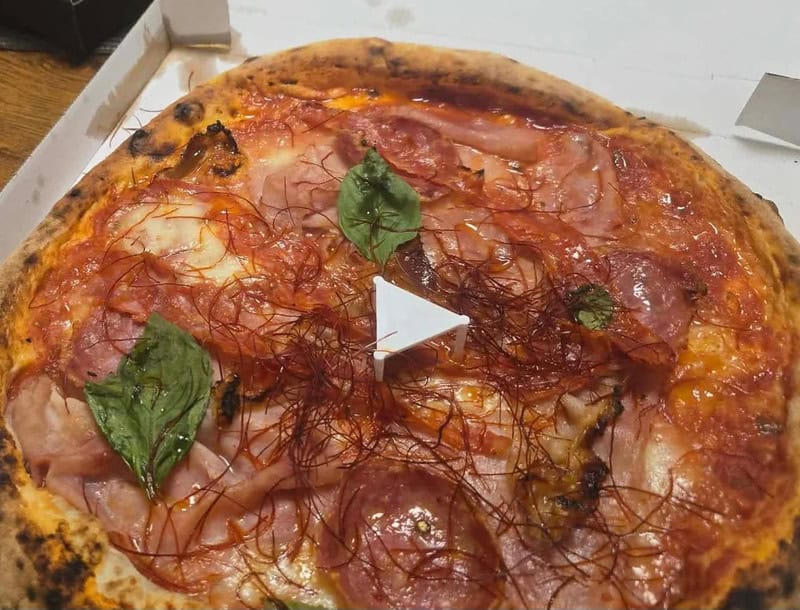 Close-up of a pizza with ham, basil, and chili threads.