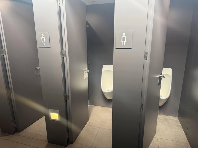 Two bathroom stalls with urinals, one open and one closed, in a public restroom.