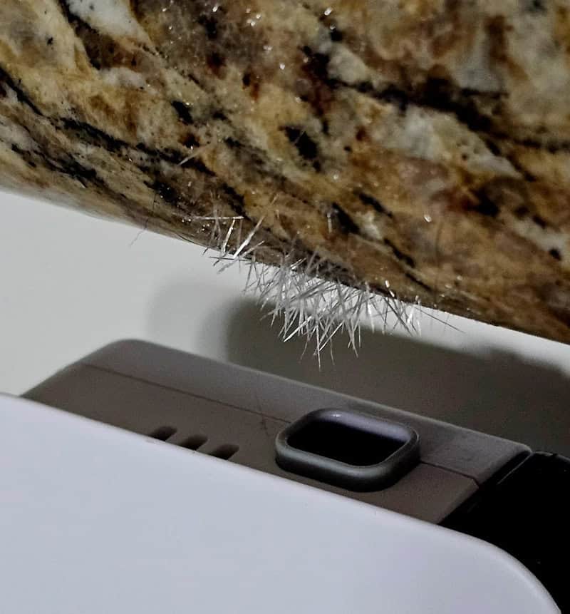 Close-up of a hairy spider on a granite surface near a smartwatch and a white device.