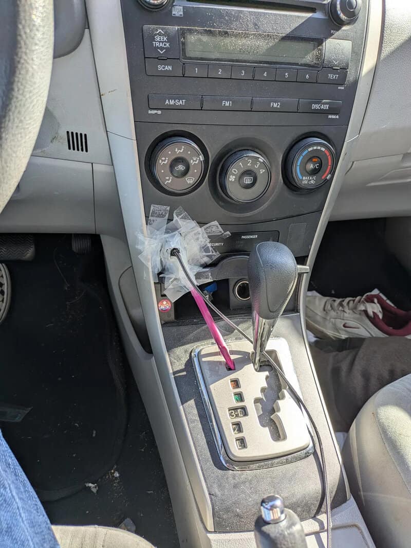 Car interior with gear shift, climate controls, and a plastic bag with a pink stick inside.