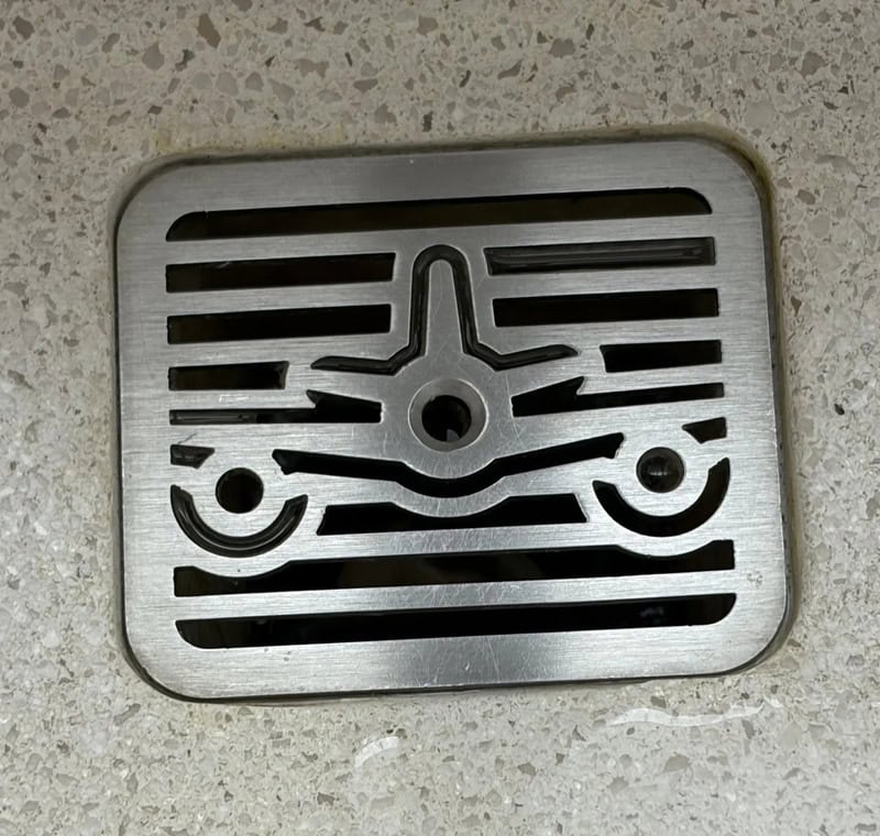 Drain cover with a face-like design on a concrete floor.