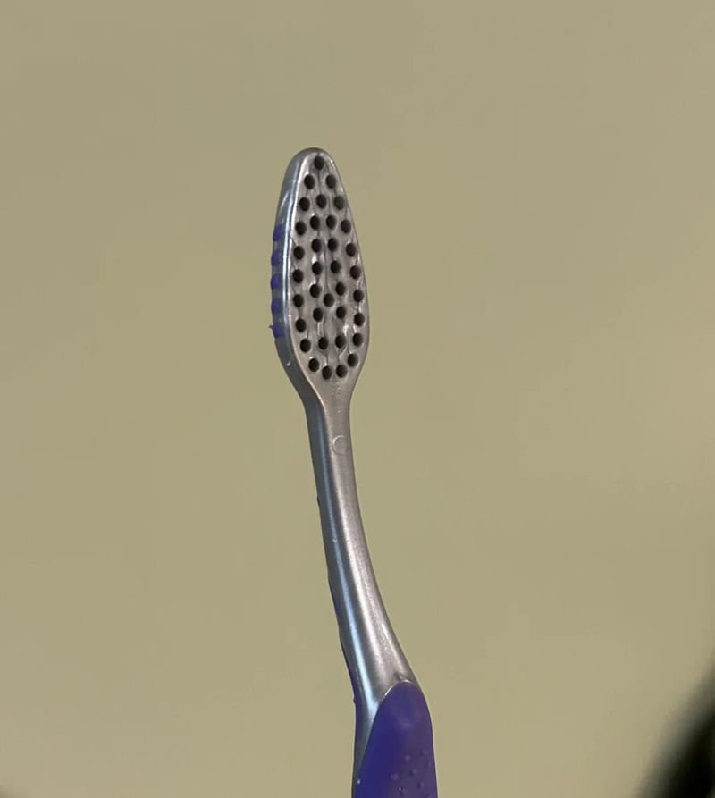 A metal toothbrush with holes in the head, against a plain background.