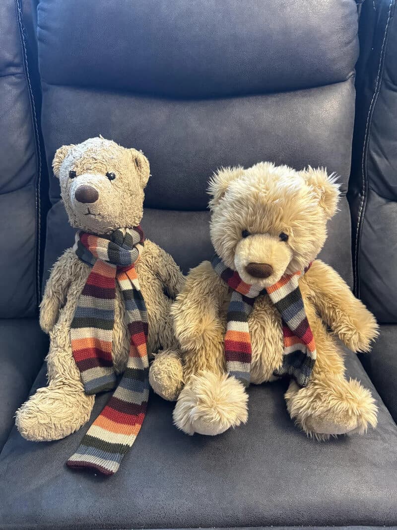 Two teddy bears with scarves sitting on a gray chair.
