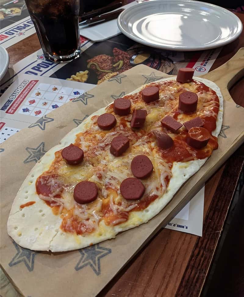 Uncooked pizza with pepperoni and cheese on a wooden board at a restaurant.