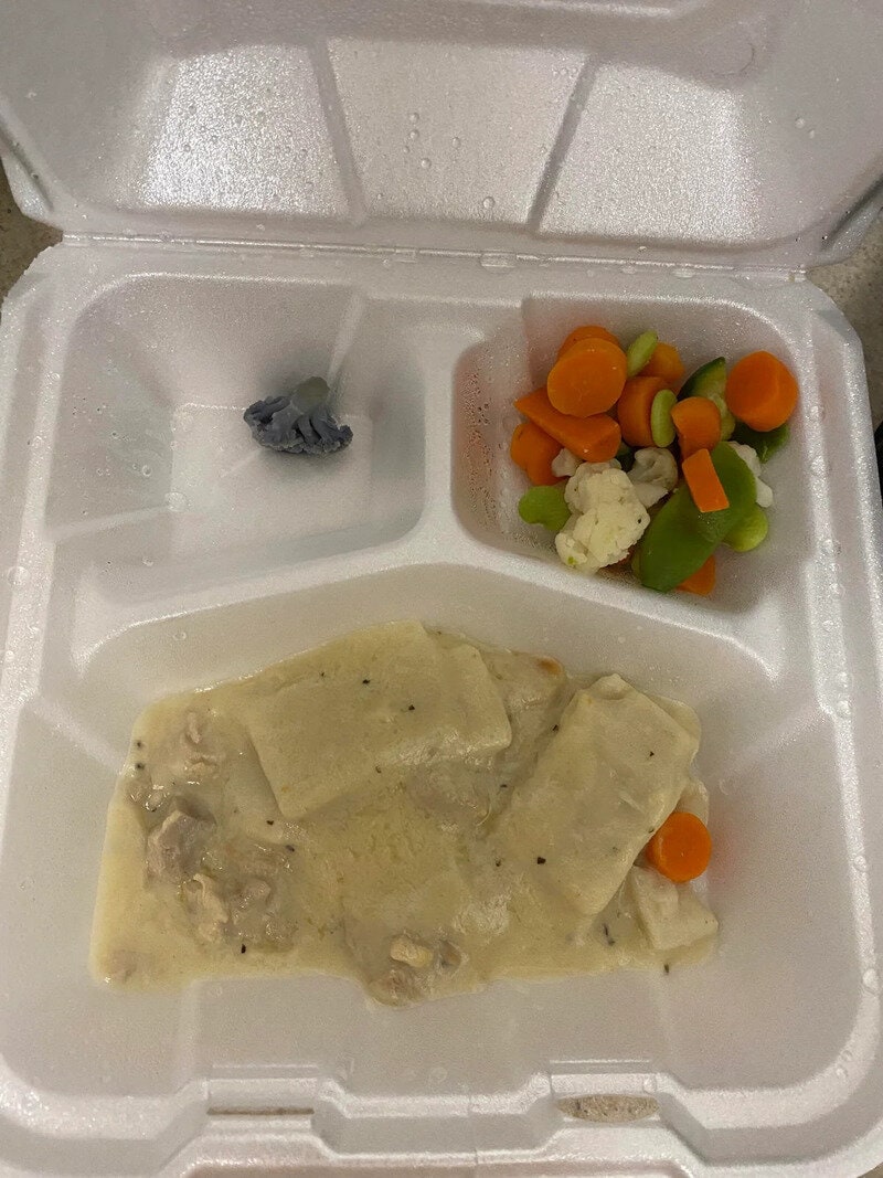 Empty food container with leftover chicken and vegetables, and a small fish in water.