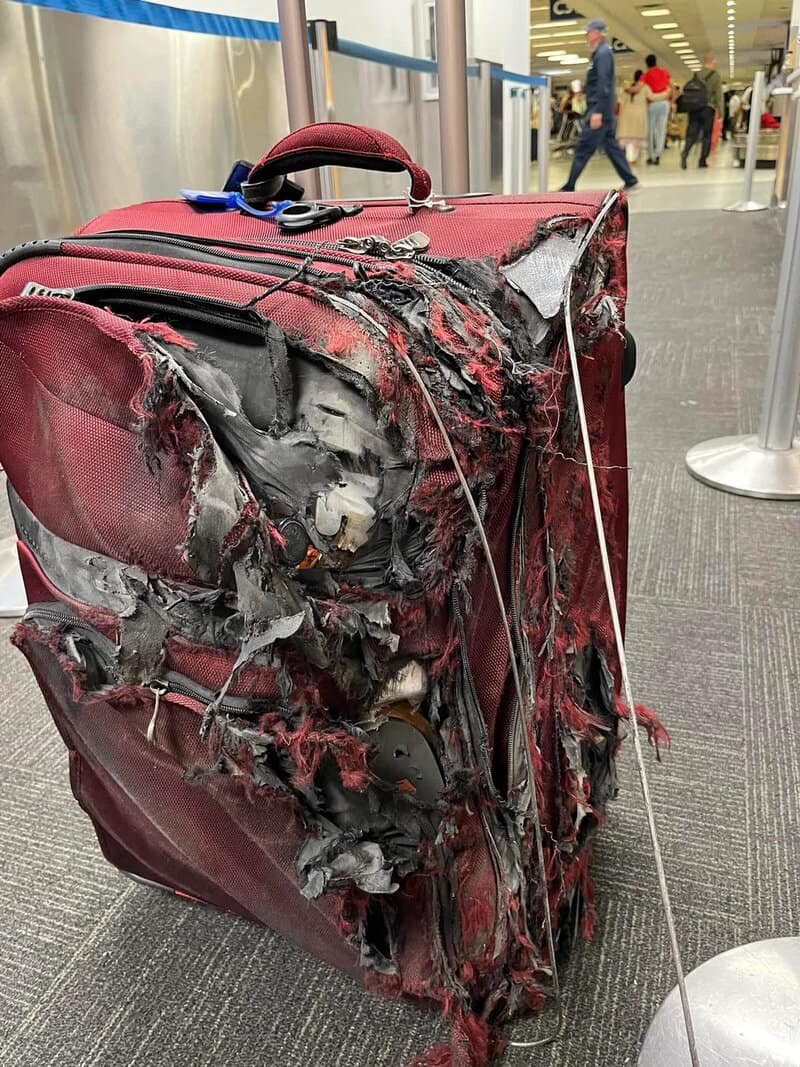 Burned and damaged red suitcase at airport terminal.