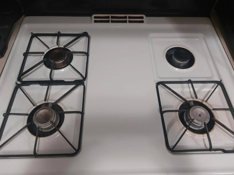 Four burners on a white stove, one with a black cap, others with metal grates.