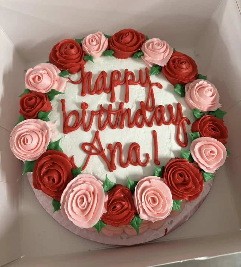 Birthday cake with pink and red roses and 'Happy birthday Ana!' written in red icing.