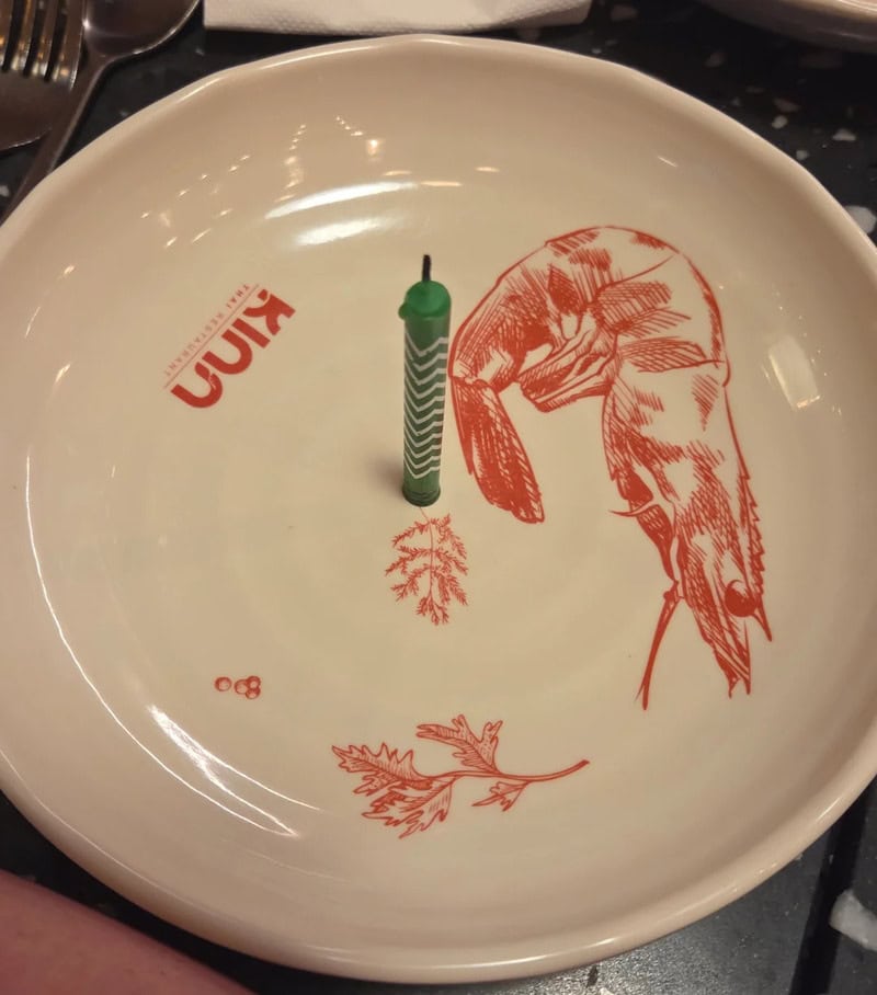 A plate with a fish illustration, a candle, and a leaf design, with the word 'Kinn' on it.