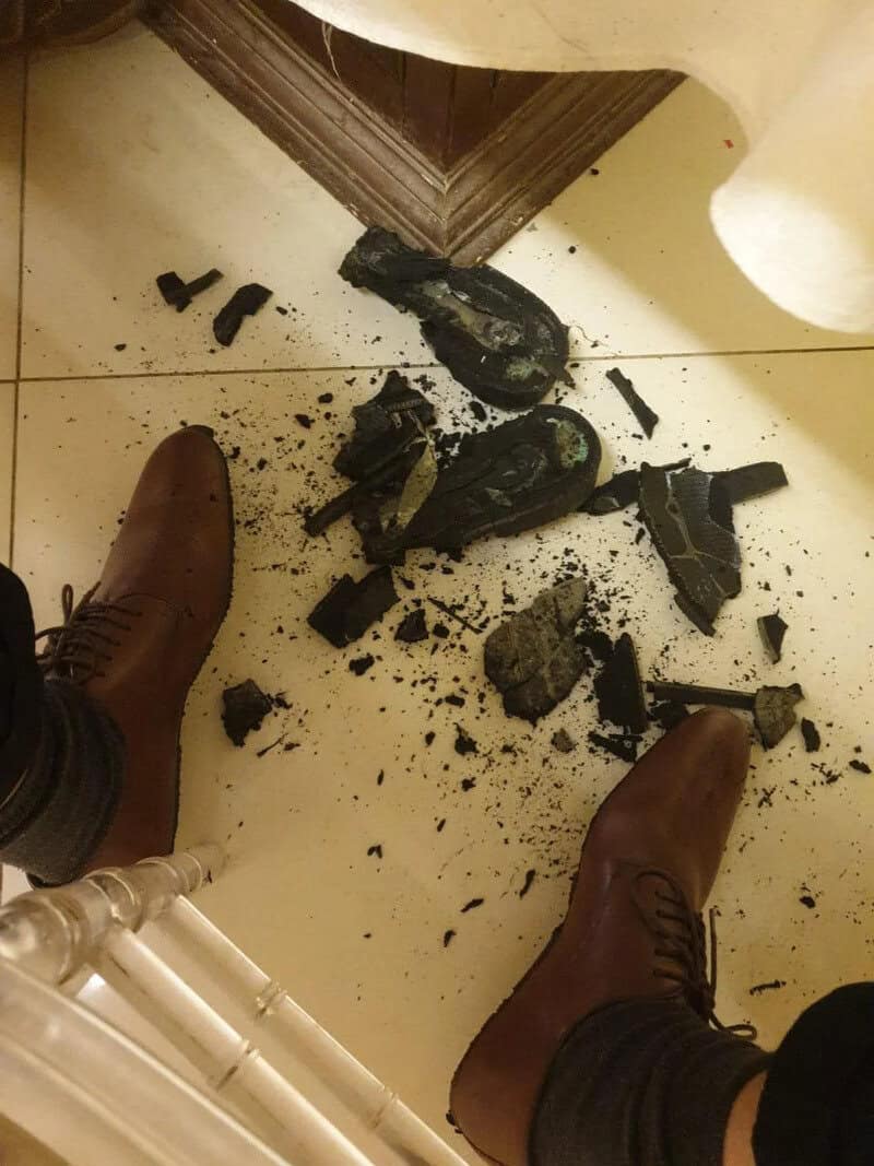 Broken shoe and scattered debris on the floor, with a person's brown boots visible.