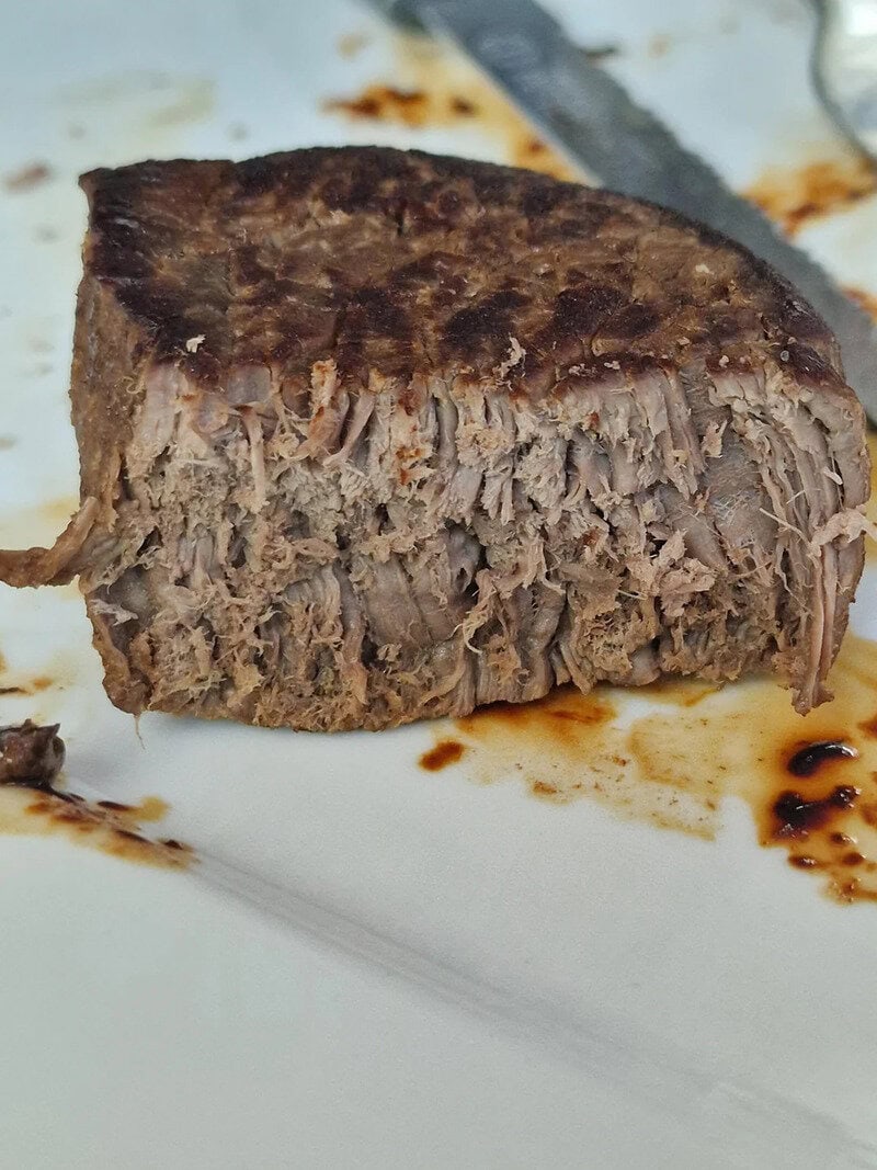 Cooked beef steak on a white plate with sauce drips.