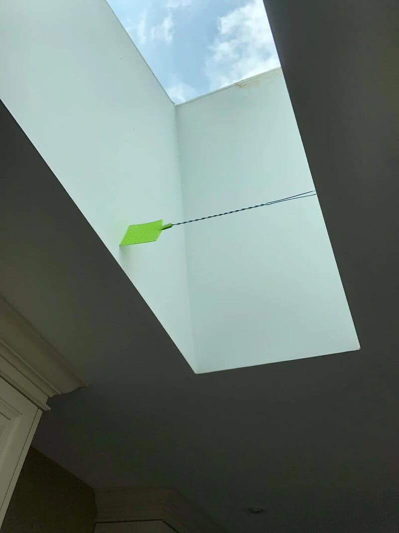 Green kite caught in skylight, hanging from string.