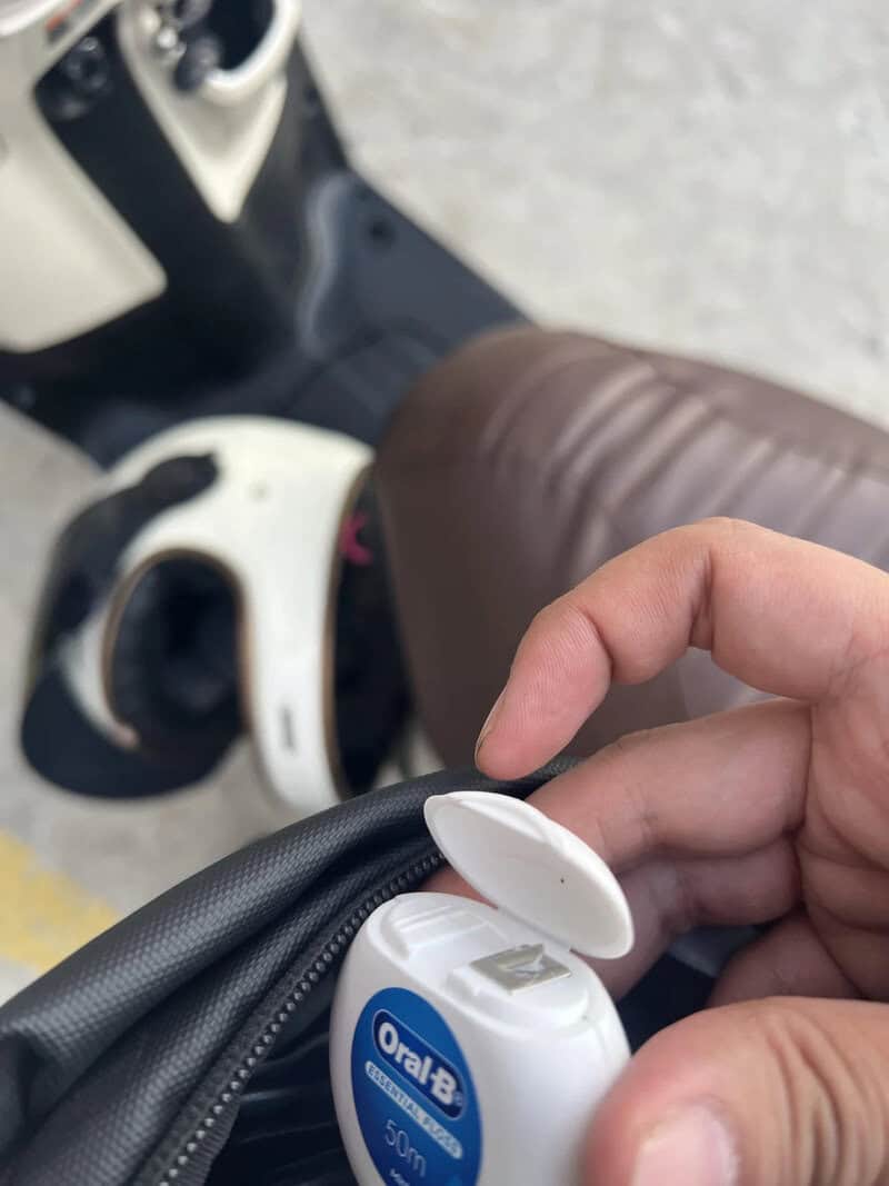 Person's hand opening a small Oral-B toothbrush container on a motorcycle seat.