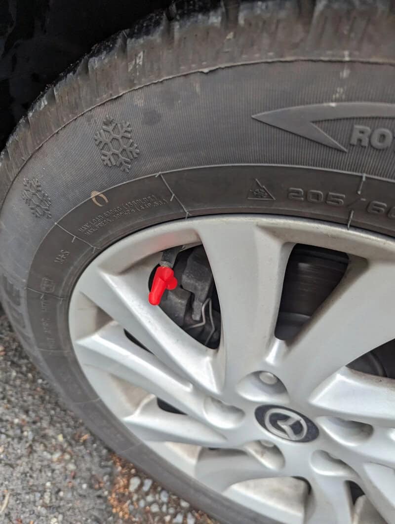 Flat tire on a car with a red valve cap, wheel on gravel surface.