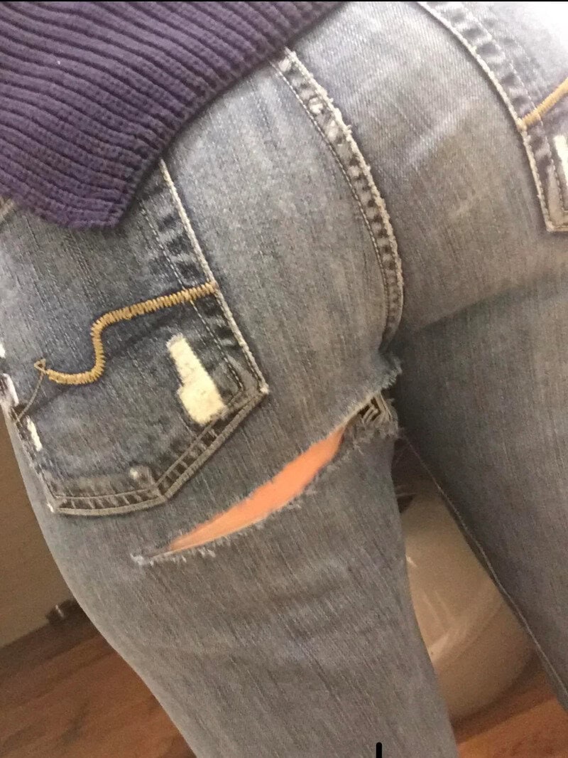 Close-up of a person wearing ripped jeans with a large tear on the back pocket.