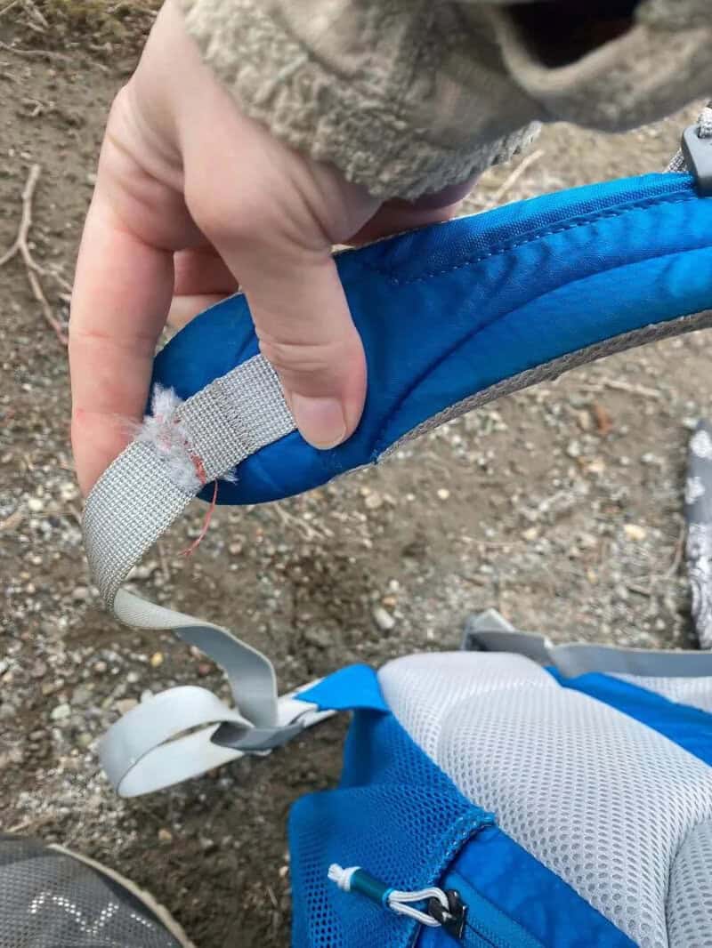 Close-up of a hand holding a damaged blue backpack strap.