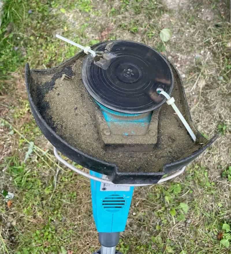 Homemade device with a black reel, sand, and tubing on a blue stand in dirt.