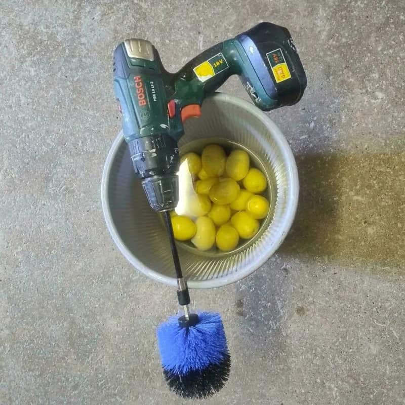 A cordless drill attached to a brush, placed over a bucket of yellow balls.