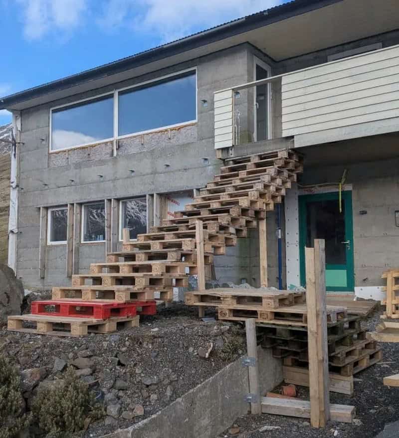 Unconventional staircase made of stacked wooden pallets leading to a second-floor balcony.