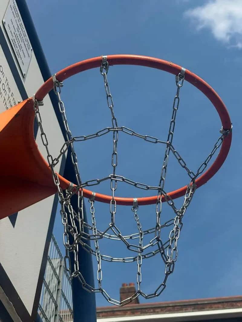 Basketball hoop with chains instead of a net under a blue sky.
