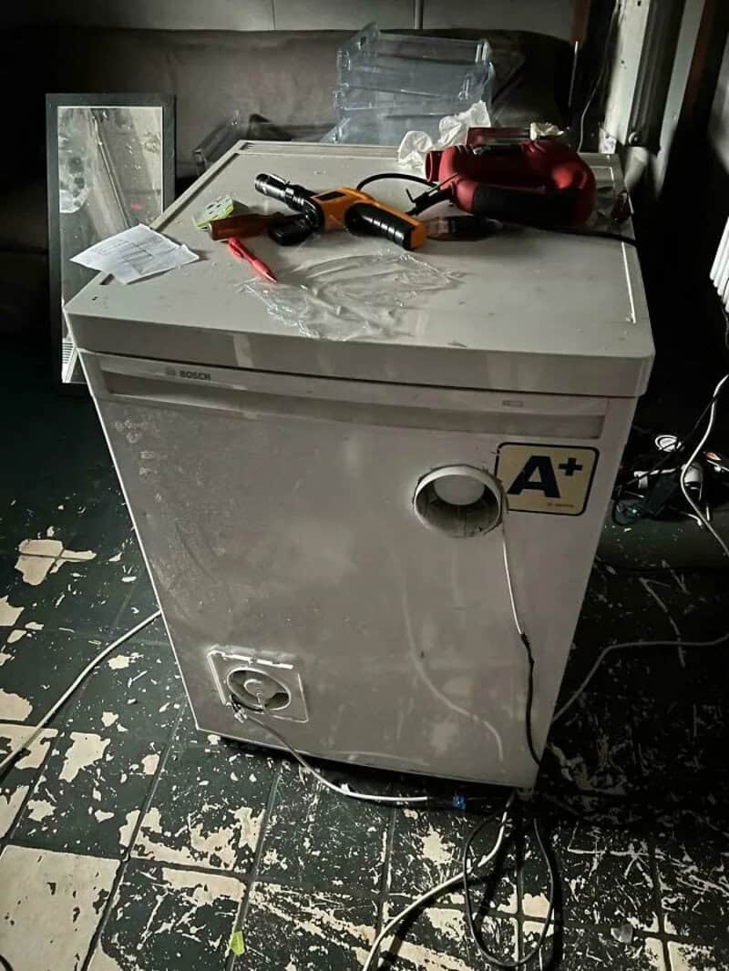 A washing machine with various tools and objects on top, in a cluttered room.