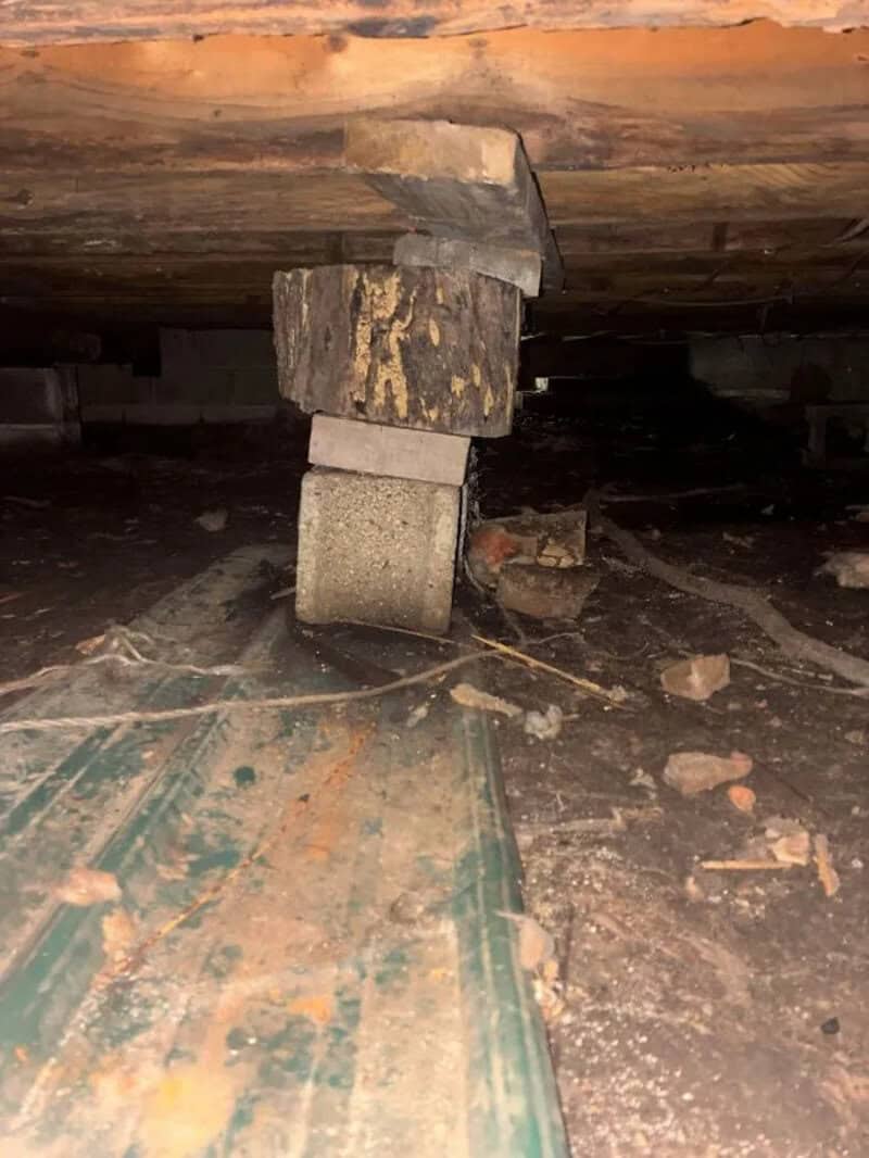 A makeshift support under a wooden structure using a block and a piece of wood.
